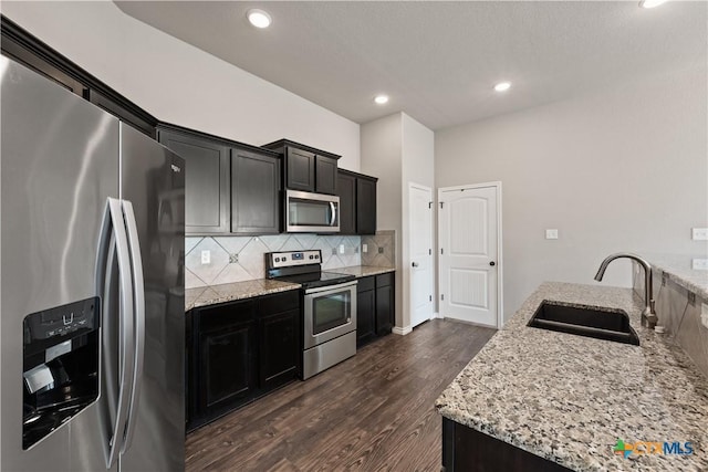 kitchen featuring light stone counters, dark wood-style flooring, stainless steel appliances, tasteful backsplash, and a sink