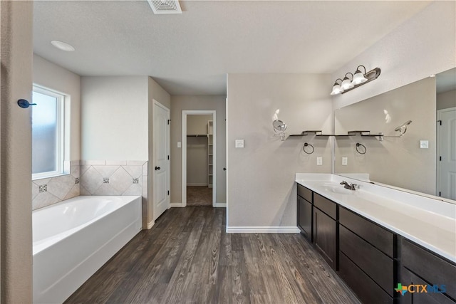 bathroom with wood finished floors, vanity, visible vents, a spacious closet, and a bath