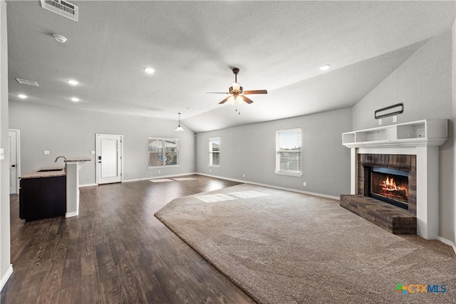 unfurnished living room with visible vents, lofted ceiling, ceiling fan, a fireplace, and a sink