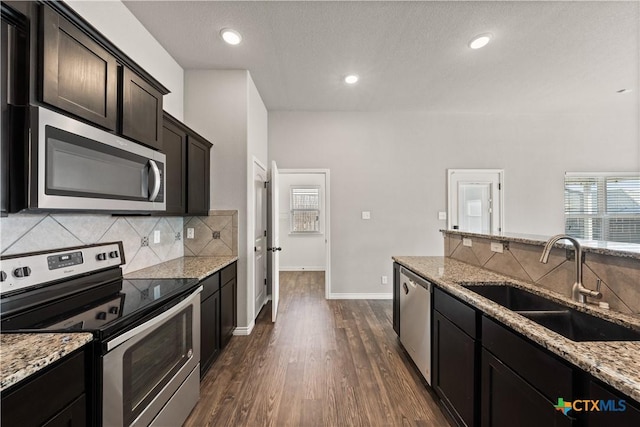 kitchen with light stone countertops, backsplash, stainless steel appliances, and a sink