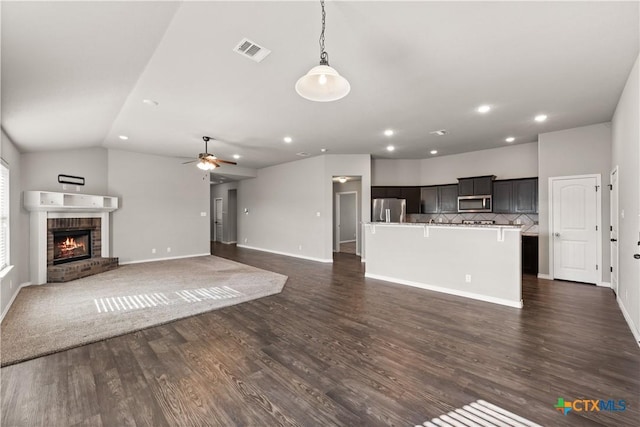 unfurnished living room with a ceiling fan, a brick fireplace, visible vents, and dark wood-style flooring