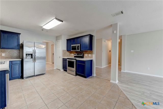 kitchen featuring blue cabinetry, appliances with stainless steel finishes, a textured ceiling, light tile patterned floors, and decorative backsplash