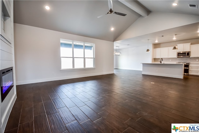 unfurnished living room featuring beam ceiling, high vaulted ceiling, sink, dark wood-type flooring, and ceiling fan with notable chandelier