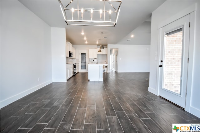 unfurnished living room featuring dark wood-type flooring, sink, and an inviting chandelier