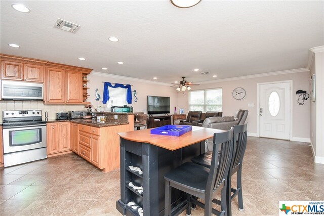 kitchen featuring stainless steel appliances, tasteful backsplash, a kitchen bar, ceiling fan, and crown molding