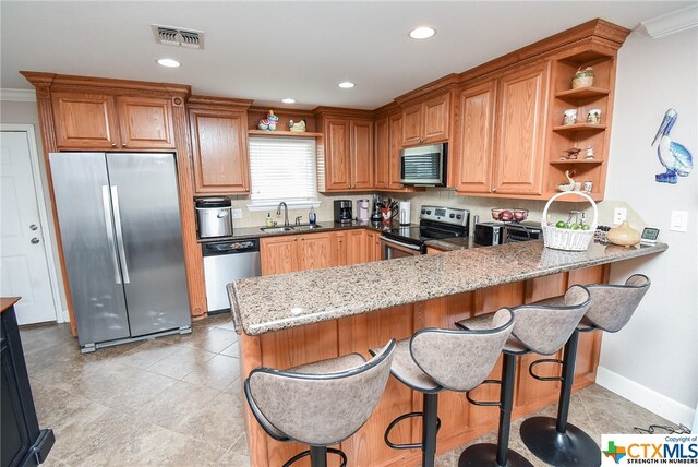 kitchen with light stone counters, ornamental molding, stainless steel appliances, sink, and kitchen peninsula