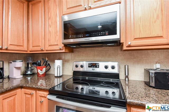 kitchen with appliances with stainless steel finishes, dark stone counters, and tasteful backsplash