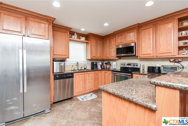 kitchen with kitchen peninsula, stainless steel appliances, sink, and light stone countertops