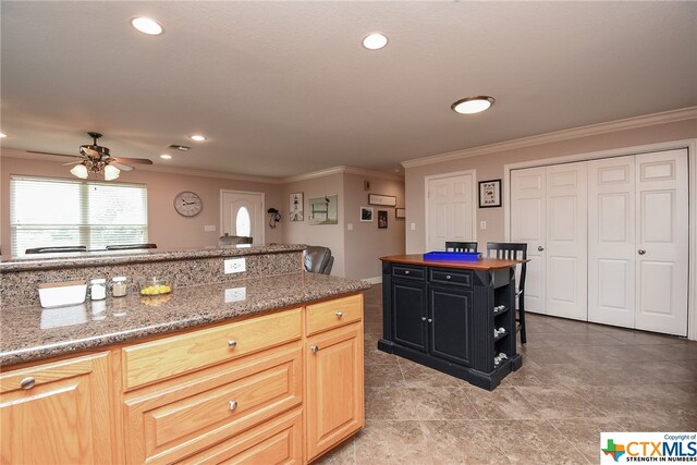 kitchen featuring light brown cabinetry, ceiling fan, crown molding, and a center island