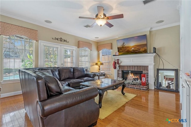 living room with a fireplace, light wood-type flooring, ceiling fan, and crown molding