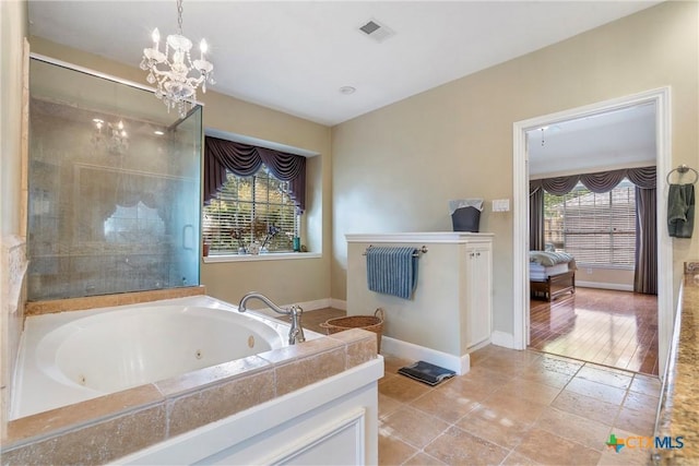 bathroom with tiled tub, plenty of natural light, and an inviting chandelier