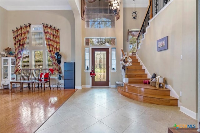 entrance foyer featuring a towering ceiling, light tile patterned floors, a notable chandelier, and ornamental molding