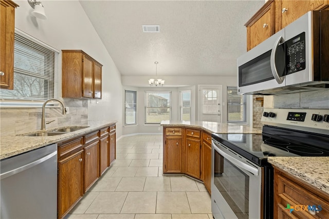 kitchen with tasteful backsplash, visible vents, appliances with stainless steel finishes, brown cabinetry, and a sink