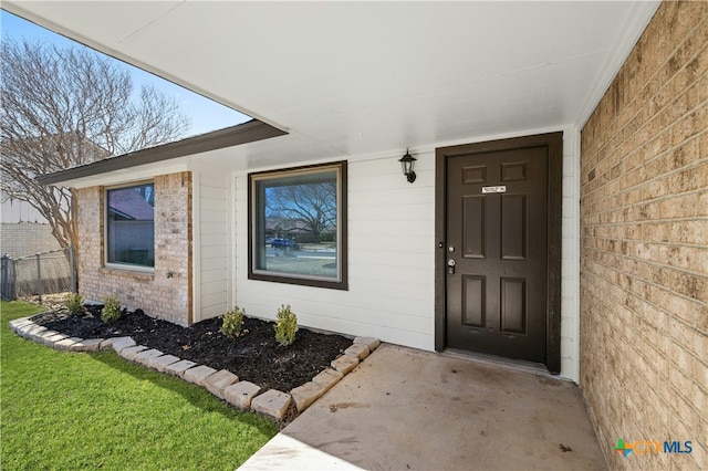 view of exterior entry with a lawn and brick siding