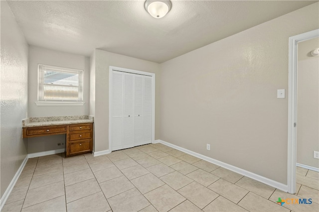 unfurnished bedroom with baseboards, a textured ceiling, built in desk, a closet, and light tile patterned flooring