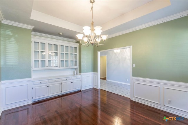 unfurnished dining area with a chandelier, dark wood-style floors, a tray ceiling, and a wainscoted wall