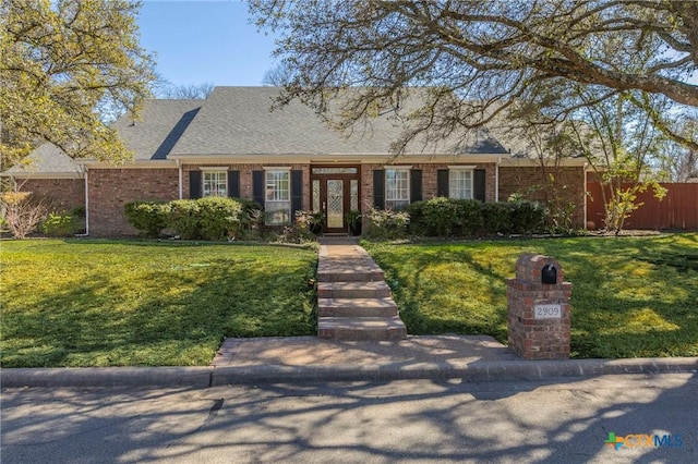 view of front facade with brick siding, a front yard, and a shingled roof