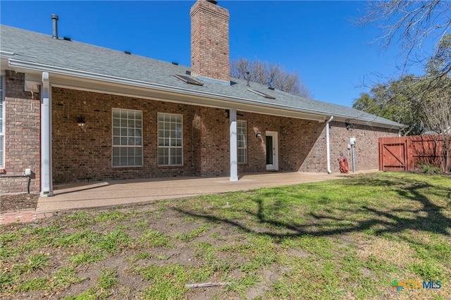 back of house featuring fence, brick siding, a chimney, a patio area, and a lawn