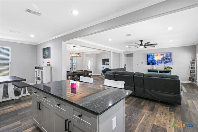 kitchen featuring visible vents, ornamental molding, dark wood finished floors, dark stone counters, and baseboards