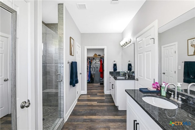 bathroom featuring a stall shower, wood finished floors, two vanities, and a sink