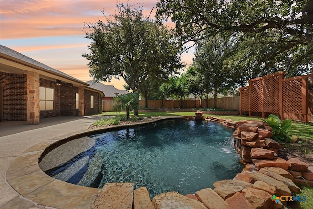 pool at dusk with pool water feature and a patio area