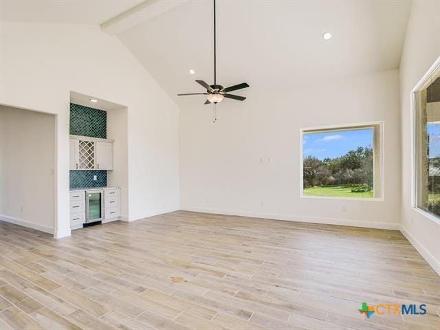 unfurnished living room with beverage cooler, high vaulted ceiling, beamed ceiling, bar area, and light hardwood / wood-style floors