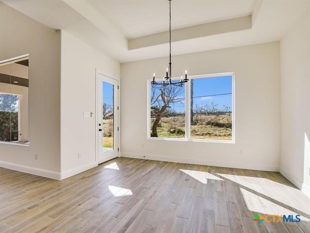 unfurnished dining area with light hardwood / wood-style floors, an inviting chandelier, a tray ceiling, and a healthy amount of sunlight