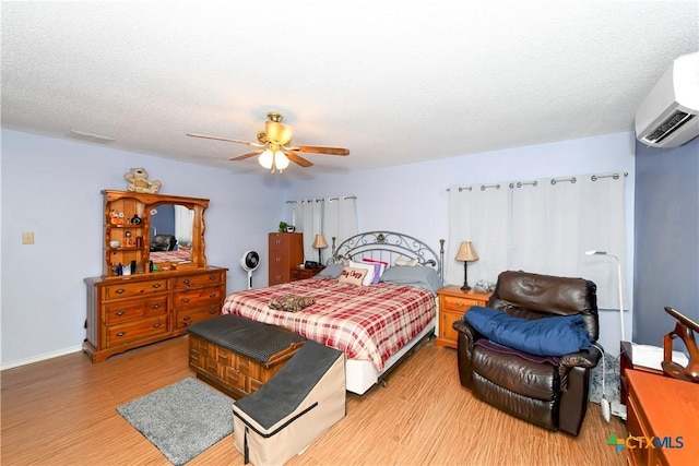 bedroom featuring ceiling fan, a textured ceiling, a wall unit AC, and light hardwood / wood-style flooring