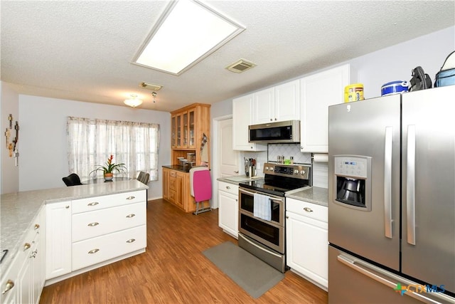 kitchen featuring tasteful backsplash, a textured ceiling, light wood-type flooring, appliances with stainless steel finishes, and white cabinets