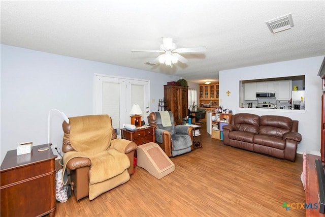 living room featuring ceiling fan, light hardwood / wood-style flooring, and a textured ceiling