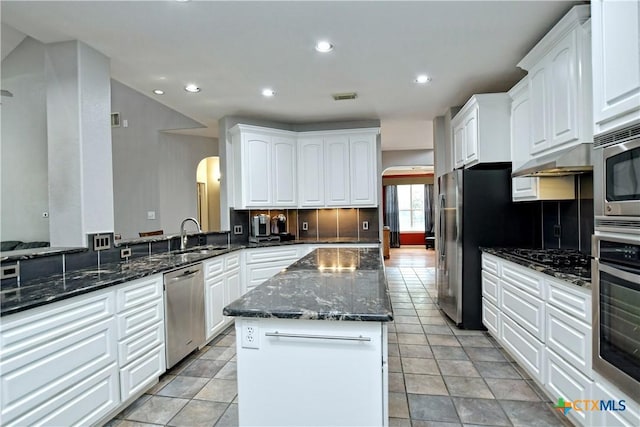 kitchen featuring visible vents, a center island, arched walkways, stainless steel appliances, and a sink