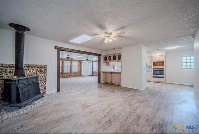 unfurnished living room featuring a wood stove, baseboards, light wood-type flooring, and ceiling fan