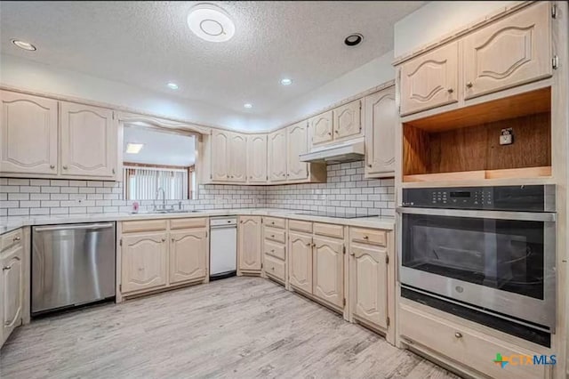 kitchen with light wood-type flooring, under cabinet range hood, a sink, stainless steel appliances, and decorative backsplash