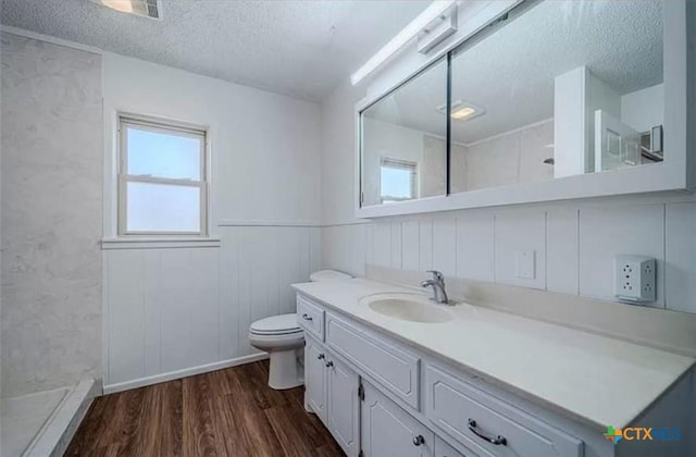 full bath featuring a wainscoted wall, a walk in shower, a textured ceiling, and wood finished floors