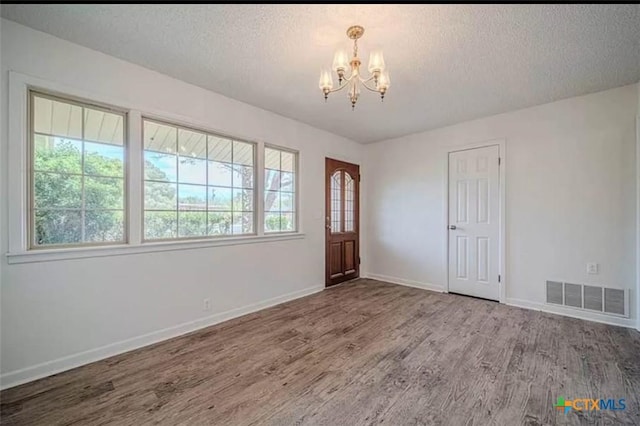 entryway featuring visible vents, baseboards, wood finished floors, a notable chandelier, and a textured ceiling