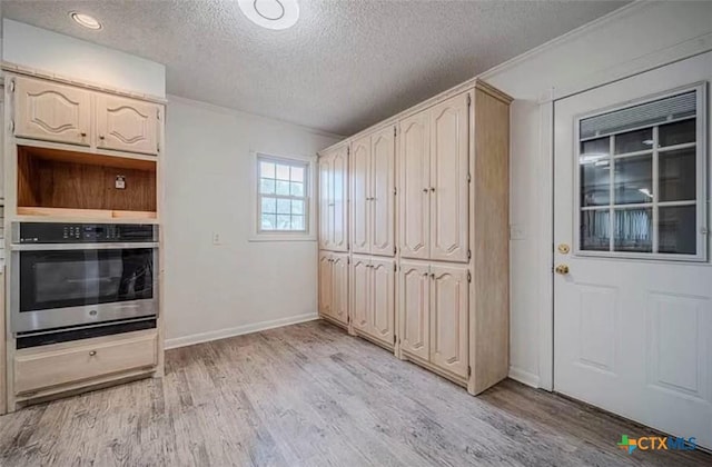 interior space with oven, light wood-type flooring, baseboards, and a textured ceiling