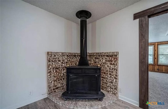 details featuring a wood stove, wood finished floors, baseboards, and a textured ceiling