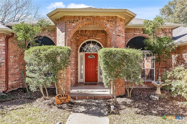 property entrance featuring brick siding and roof with shingles