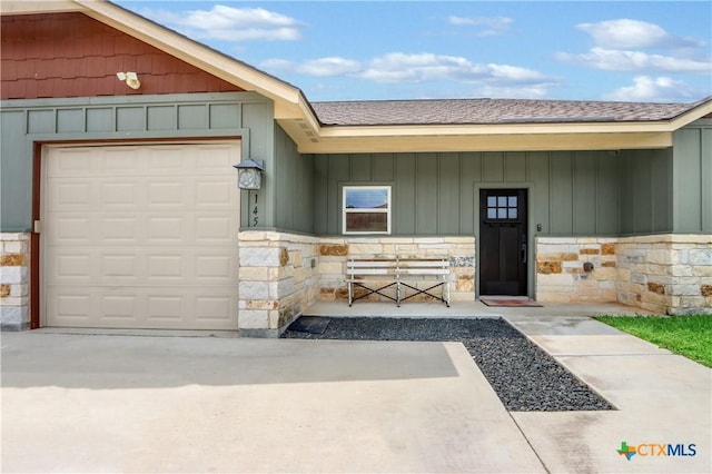doorway to property featuring a garage, a shingled roof, stone siding, and board and batten siding
