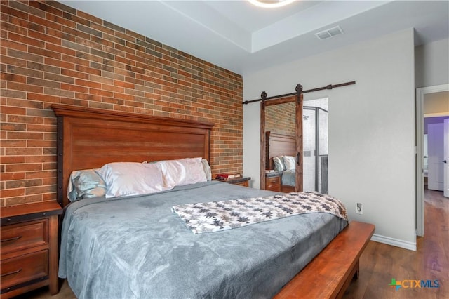 bedroom with wood finished floors, a barn door, visible vents, brick wall, and baseboards
