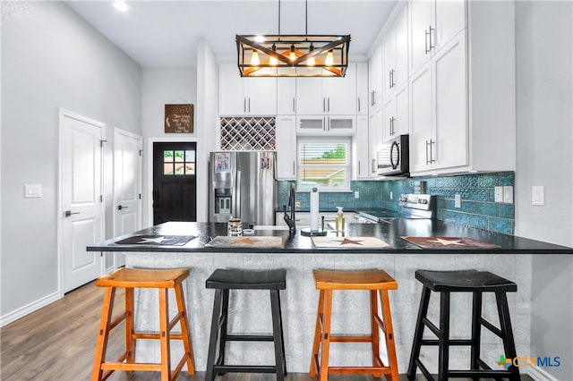 kitchen with white cabinetry, a peninsula, backsplash, dark countertops, and stainless steel appliances