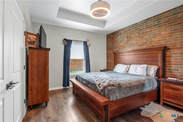 bedroom with baseboards, a raised ceiling, brick wall, and wood finished floors