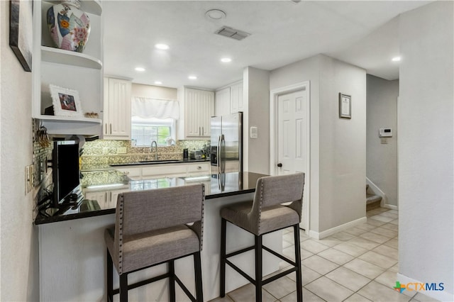 kitchen with tasteful backsplash, light tile patterned flooring, stainless steel fridge, sink, and white cabinets