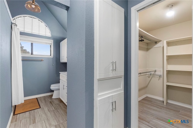 bathroom featuring a shower with curtain, wood finished floors, baseboards, a spacious closet, and toilet