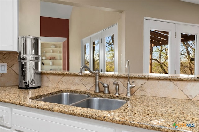 interior details featuring a sink, decorative backsplash, light stone countertops, and white cabinets