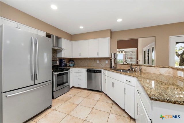 kitchen featuring backsplash, white cabinets, stainless steel appliances, wall chimney exhaust hood, and a sink