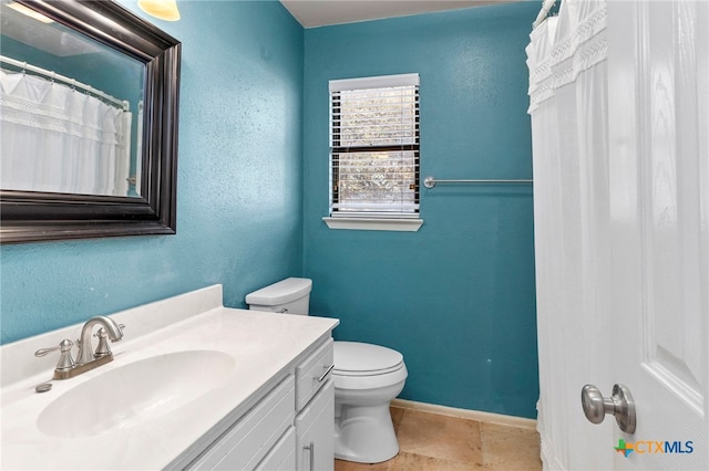 bathroom with vanity, toilet, a textured wall, and baseboards