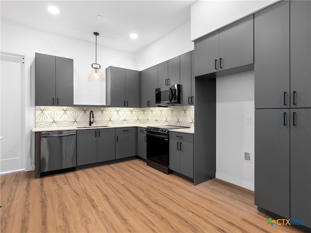 kitchen with light wood-style flooring, decorative light fixtures, a sink, stainless steel appliances, and backsplash