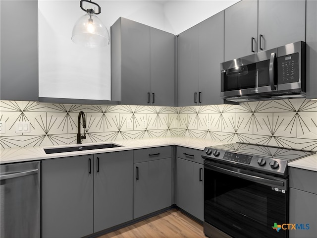 kitchen featuring appliances with stainless steel finishes, gray cabinets, a sink, and tasteful backsplash