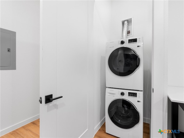 laundry area featuring light wood finished floors, stacked washing maching and dryer, laundry area, electric panel, and baseboards